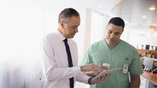 2 men, one in scrubs, looking down at a tablet